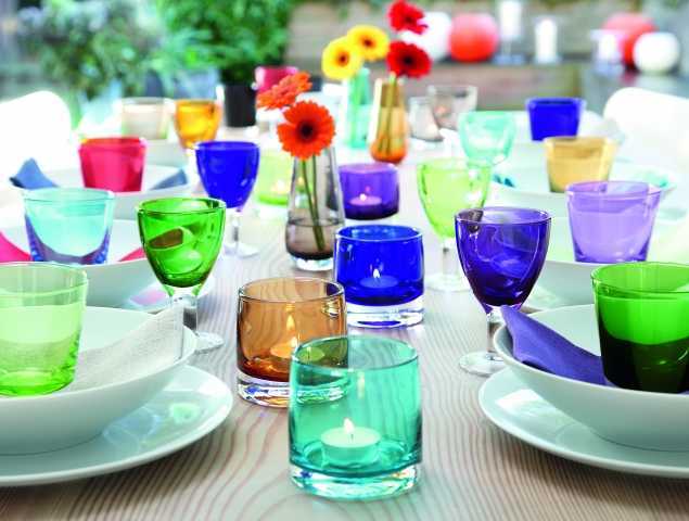 פמוטים נמוכים, וואזות וכוסות במגוון צבעים עשויים מזכוכית בעבודת יד בשילוב עם צלחות מפורצלן